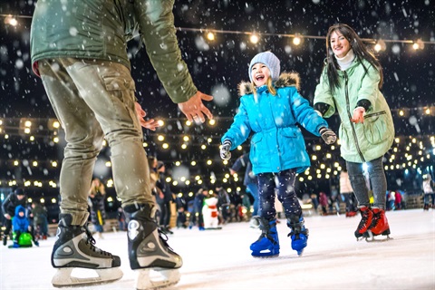 Girls skating on an ice rink with a string of lights above. 