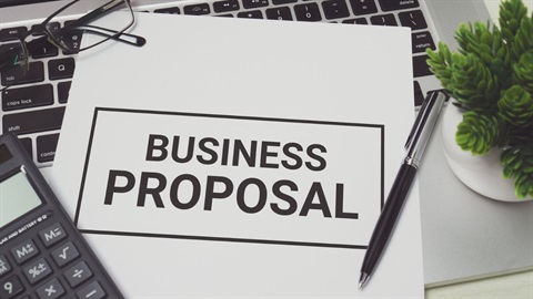 Office supplies on a desk, including a paper that says, in big letters: BUSINESS PROPOSAL.