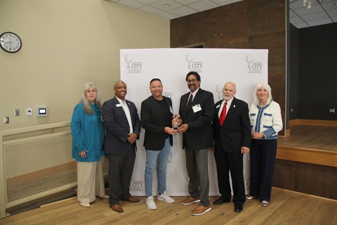 Six people stand in front of a Commerce City background. 