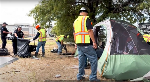 Workers remove a tent and other items from an enceampment. 