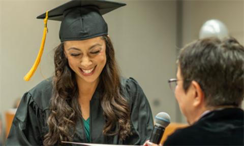 A woman wearing a cap and gown smiles. 