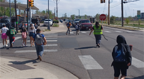 A crossing guard crosses kids across a street. 