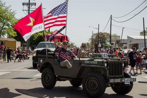 People ride on a military Jeep in a parade. 