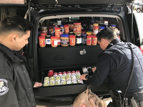 Police officers load the back of a police car with peanut butter and jelly materials. 