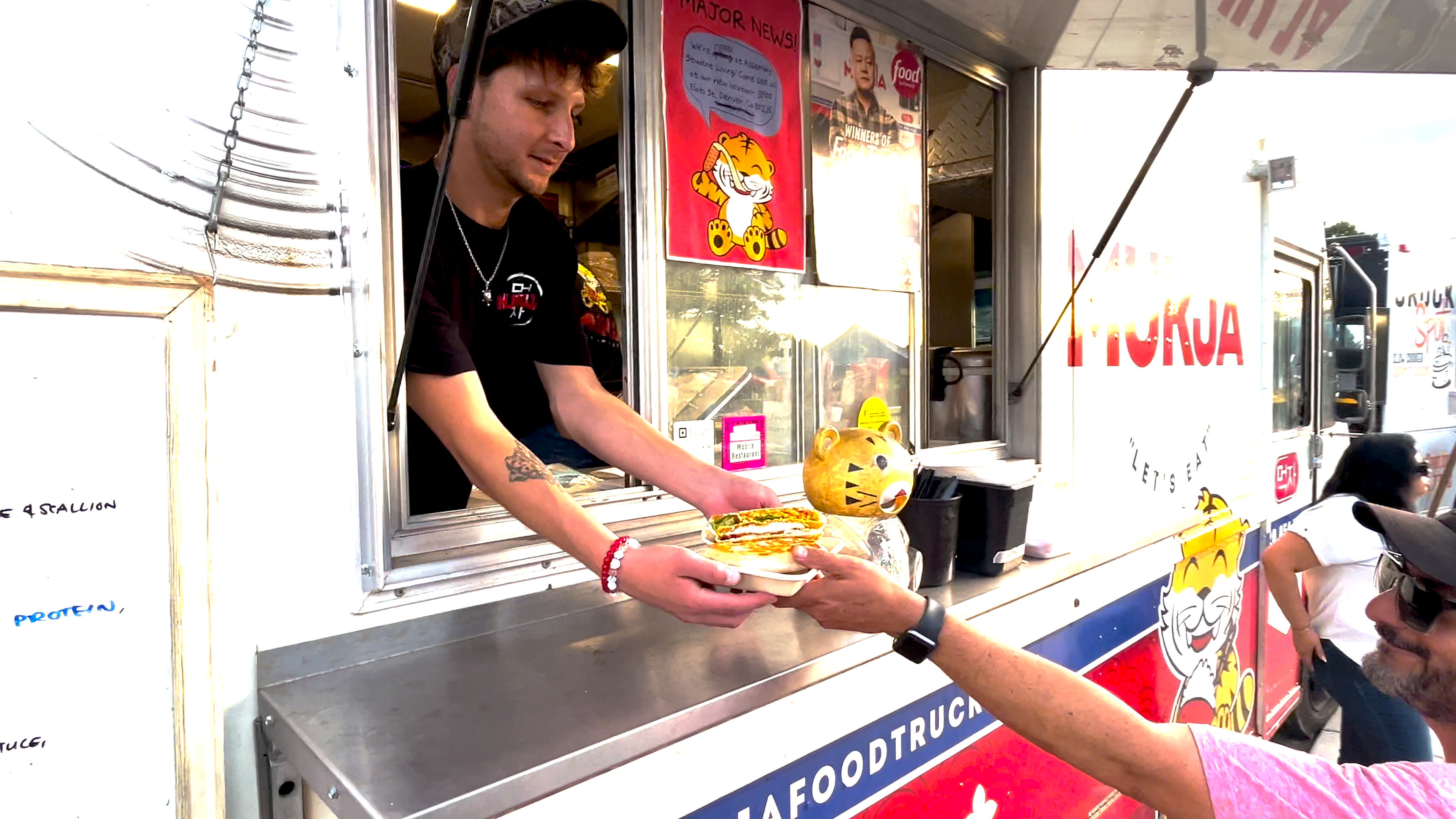 A man in a food truck a hands a person food. 