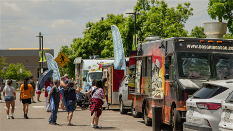 People stand in front of a line of food trucks. 