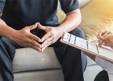 Man sitting with fingers pressed together at a doctor's office. 