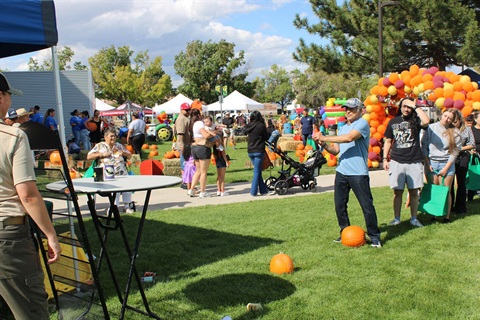 People at a booth playing games. Orange, fall colored baloons in the background. 