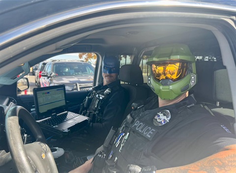 Police officers sit in their police car wearing Halloween masks. 