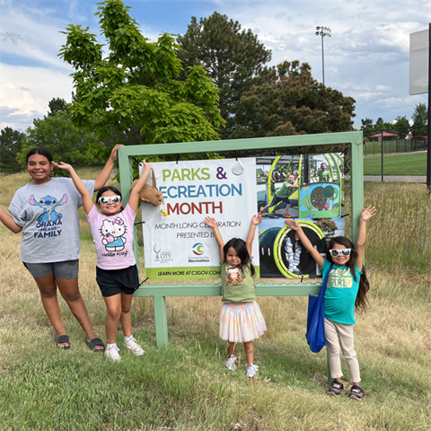 Four girls standing with their hands up in front of a banner that reads Parks, Recreation, and Golf Month