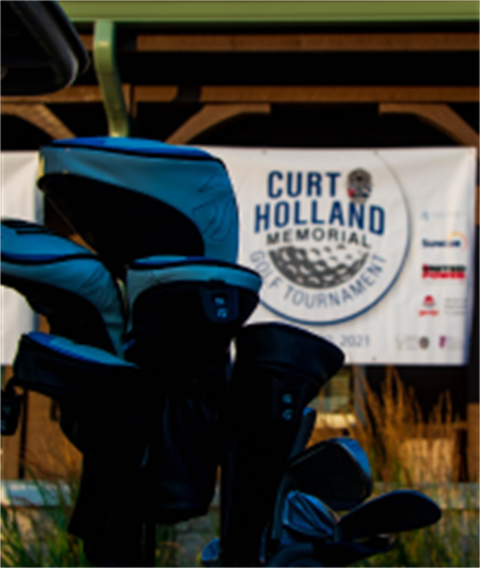 Golf clubs in front of Curt Holland Memorial tournament sign.