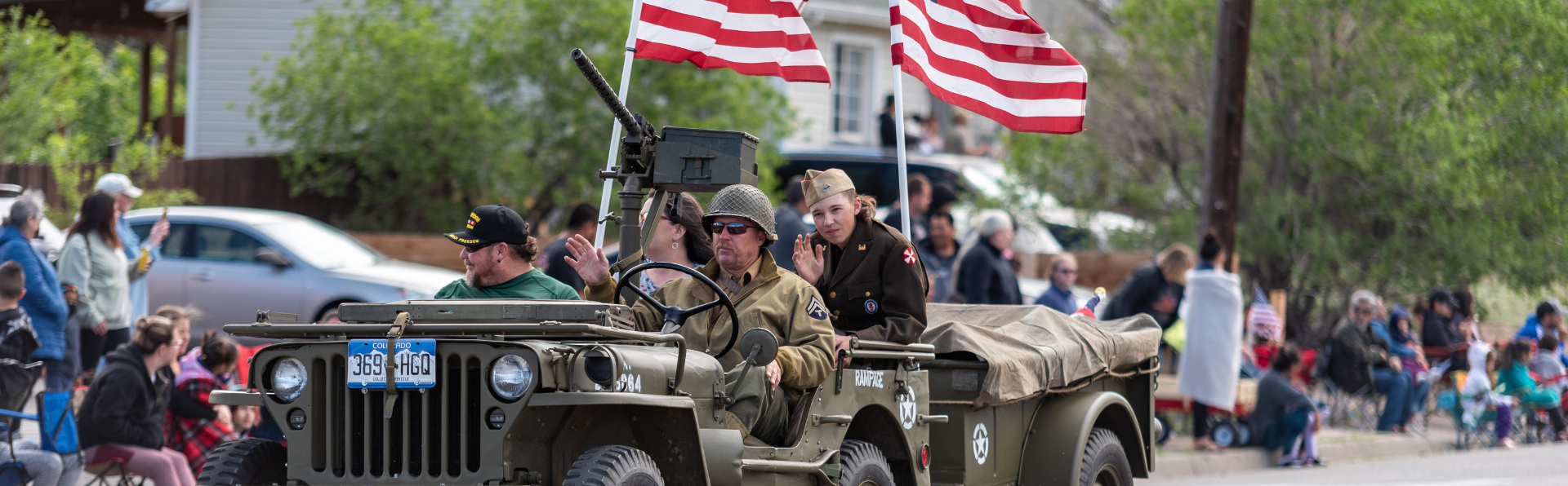People drive an old military vehicles in a parade waving American flags. 